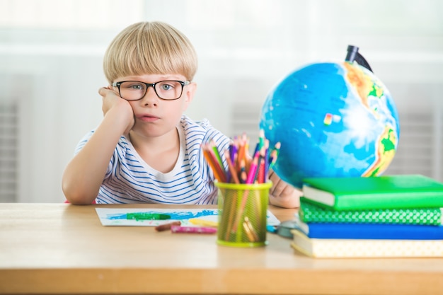 Bambino stanco di imparare. Studente infelice. Piccolo scolaretto esausto. Ragazzo in classe. Kid fare i compiti.