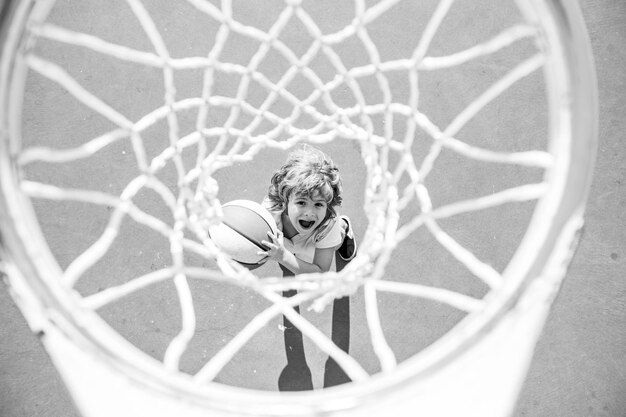 Bambino stupito che gioca a basket tenendo la palla con la faccia felice.