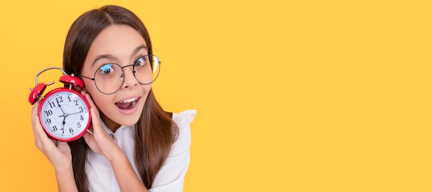 Bambino stupito in uniforme scolastica e occhiali ascolta la sveglia che squilla mostrando il tempo stupore Bambino adolescente con sveglia poster orizzontale Banner intestazione spazio copia