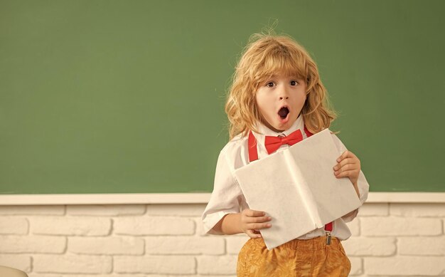 Bambino stupito nello studio del farfallino nella classe della scuola con lo spazio della copia del taccuino per tornare a scuola