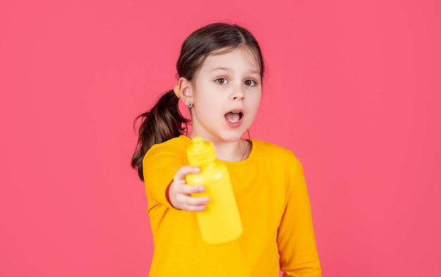 Bambino stupito tenere una bottiglia d'acqua su sfondo rosa