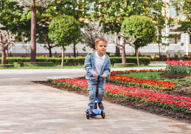 Bambino su uno scooter nel parco Un ragazzino guida uno scooter in una giornata di sole Sport attivi per bambini in età prescolare