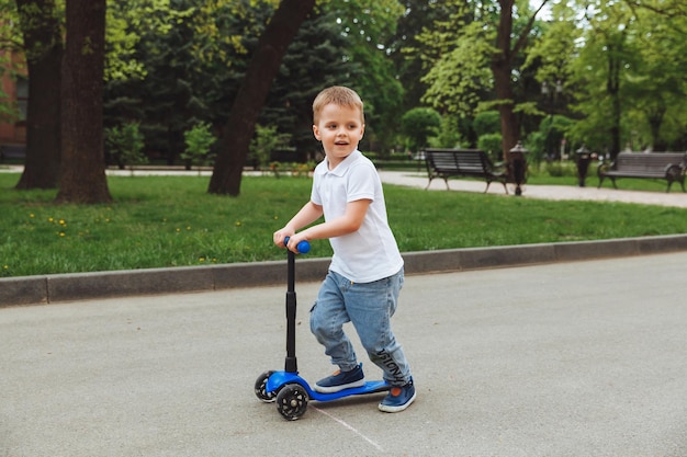 Bambino su uno scooter nel parco Un ragazzino guida uno scooter in una giornata di sole Sport attivi per bambini in età prescolare