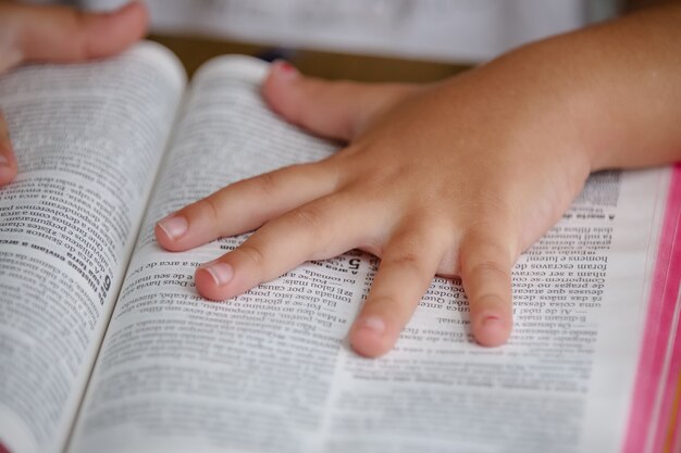 Bambino sul tavolo che legge la Sacra Bibbia e la sfoglia