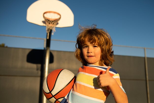 Bambino sveglio che gioca a basket Ritratto di bambino sportivo felice pollici in su