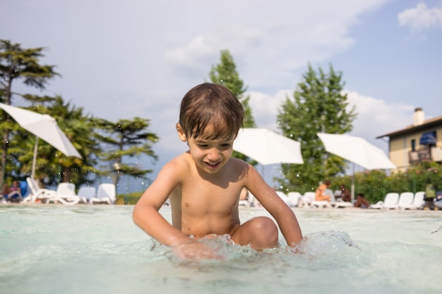 Bambino sveglio del bambino del ragazzino che spruzza in piscina divertendosi attività per il tempo libero