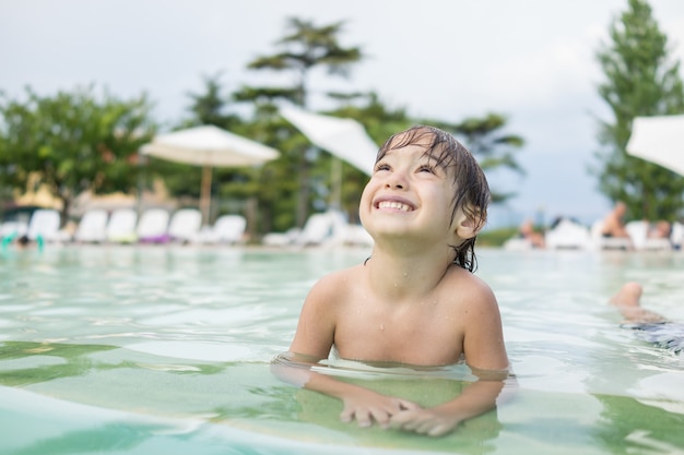 Bambino sveglio del bambino del ragazzino che spruzza in piscina divertendosi attività per il tempo libero