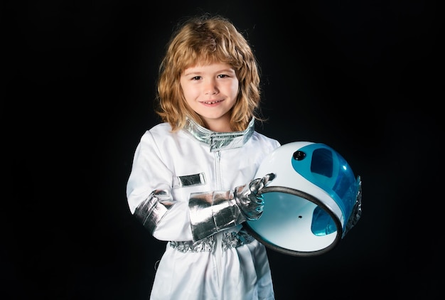 Bambino sveglio dell'astronauta del ragazzino in tuta spaziale che tiene il casco su priorità bassa nera