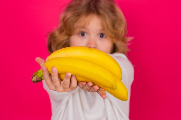 Bambino tenere banana in studio Ritratto in studio di ragazzo carino con banane isolate su sfondo rosso