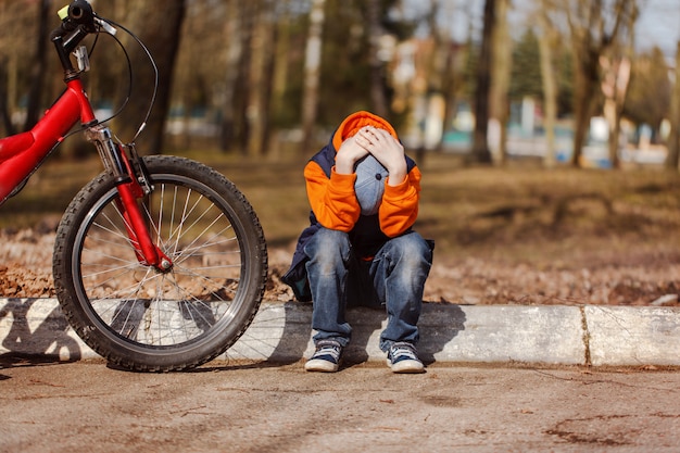 Bambino triste che si siede vicino a una bicicletta rotta