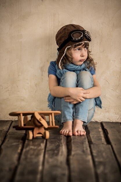 Bambino triste con l'aeroplano di legno del giocattolo che si siede sul pavimento