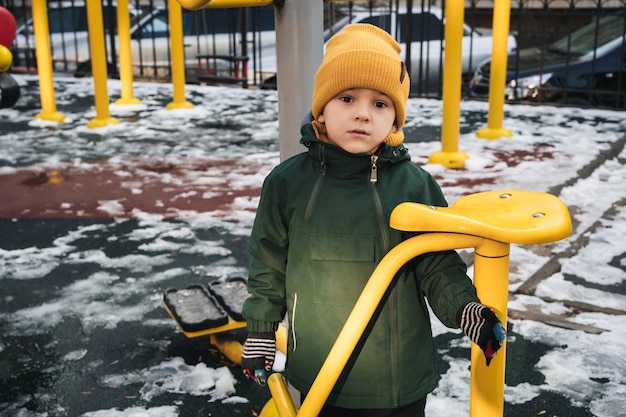 Bambino triste e solitario ragazzo che gioca sul parco da gioco da solo nel parco in inverno