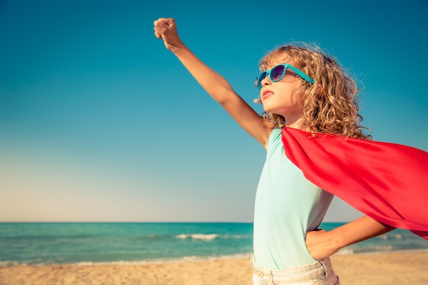 Bambino vestito da supereroe che alza il braccio sulla spiaggia