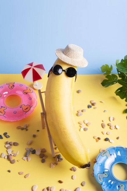 Banana con cappello e occhiali da sole sulla spiaggia con cerchi gonfiabili e ombrellone