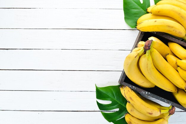 Banana con foglie verdi su un tavolo di legno bianco Frutti tropicali Vista dall'alto Spazio libero per la copia