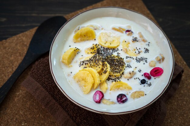 Banana di granola fresca con latte in una ciotola bianca su sfondo marrone cosparsa di semi di chia