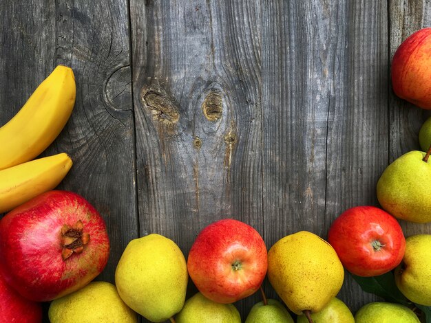 Banana, melograno, mela, pera su fondo di legno grigio