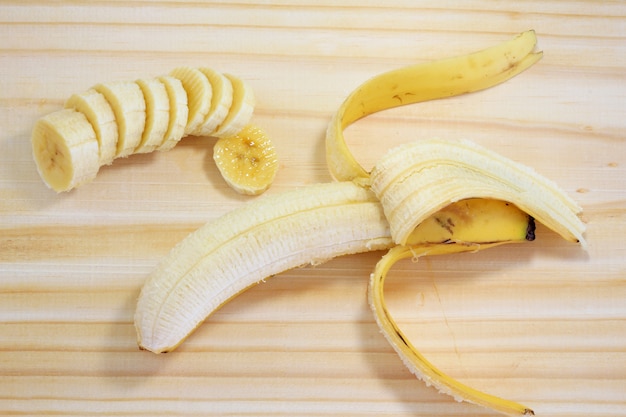 Banana sbucciata su legno accanto alla banana affettata, vista dall&#39;alto