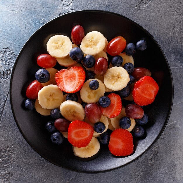 Banane, fragole, uva e mirtilli a fette in un piatto nero