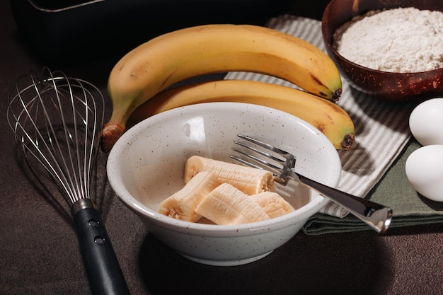 Banane sbucciate e rotte in una ciotola di ceramica ingrediente per cucinare il pane alla banana su sfondo marrone
