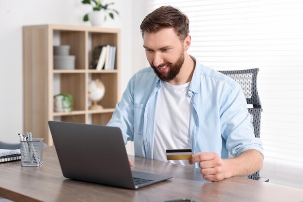 Banca online Giovane felice con carta di credito e portatile che paga l'acquisto al tavolo all'interno