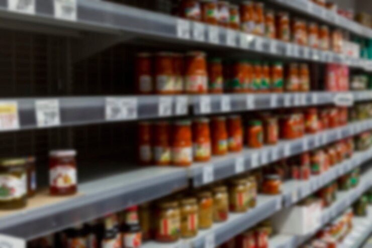 Banche con cibo in scatola sugli scaffali del negozio Fame e panico sfocati