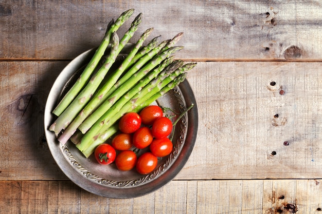 Banches di asparagi e pomodori verdi freschi in un piatto del metall su fondo di legno