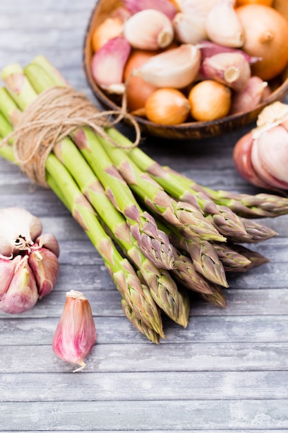 Banches di asparagi verdi freschi, aglio, su fondo in legno