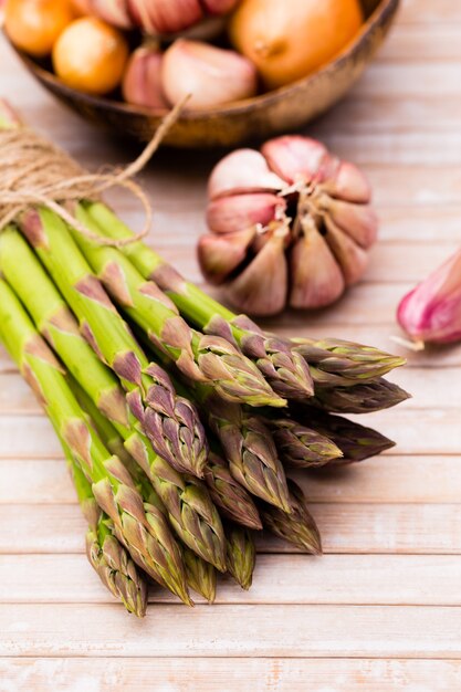 Banches di asparagi verdi freschi, aglio, su sfondo di legno, vista dall'alto