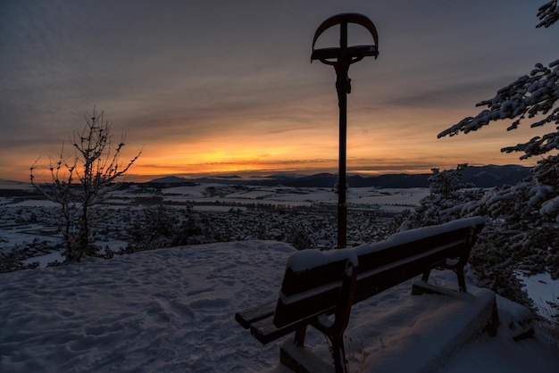 Banco solitario vuoto e croce con Gesù Cristo in una fredda mattina d'inverno nevoso nel villaggio Martincek Slovacchia