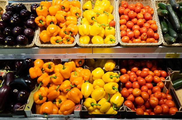 Bancone del supermercato con cestini di vimini e scatole di cartone con pomodori, zucche, peperoni e melanzane arancioni e gialli