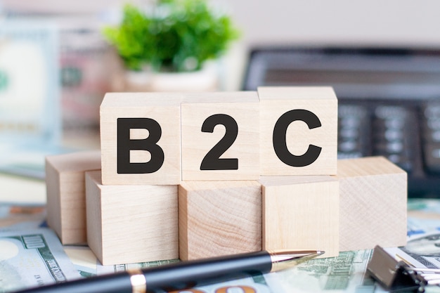 Banconota in dollari con calcolatrice e parola B2C. Banconote e cubetti di legno con lettere. Concetto con blocchi di legno e calcolatrice. B2C - Business-to-consumer.
