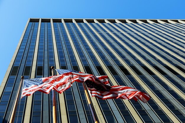 Bandiera americana che soffia nel vento contro un edificio commerciale con finestre e cielo blu con nuvole