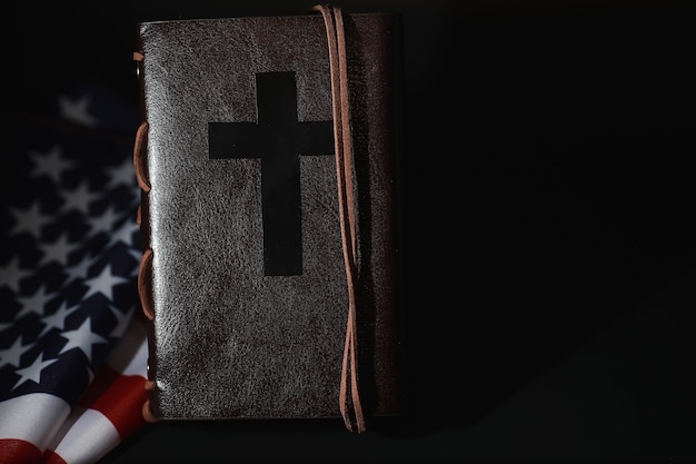 Bandiera americana e libro della Sacra Bibbia su uno sfondo a specchio. Simbolo degli Stati Uniti e della religione. Bibbia e bandiera a strisce su sfondo nero.