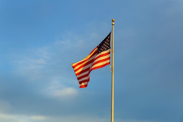 Bandiera americana sul pennone che sventola nel vento contro il cielo blu delle nuvole