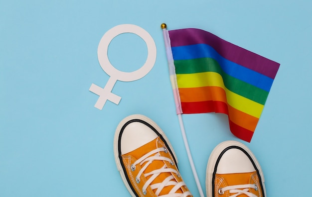 Bandiera arcobaleno LGBT e scarpe da ginnastica, simbolo femminile su sfondo blu. Tolleranza, libertà, parata gay. Vista dall'alto