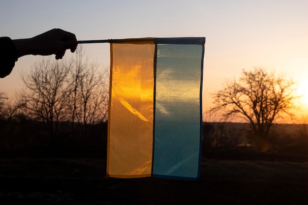 Bandiera blu gialla dell'Ucraina in mano contro il cielo al tramonto