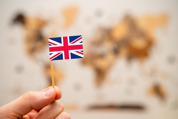 Bandiera britannica nella mano dell'uomo sullo sfondo della mappa del mondo