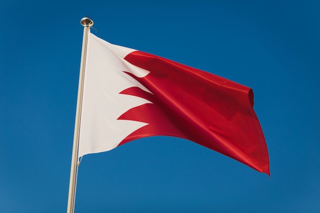 Bandiera del Bahrain rossa e bianca, capitale Manama. Bandiera nazionale sull'asta della bandiera davanti a cielo blu