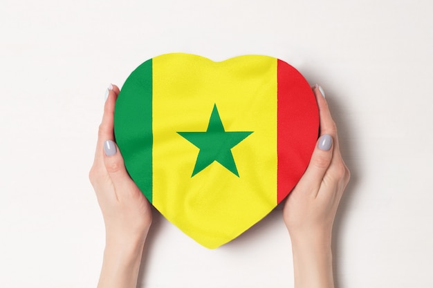 Bandiera del Senegal su una scatola a forma di cuore in mani femminili. sfondo bianco