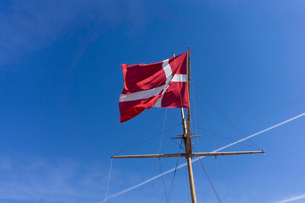 Bandiera della Danimarca su un albero di nave che rinuncia contro un cielo blu chiaro