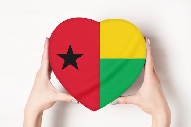 Bandiera della Guinea-Bissau su una scatola a forma di cuore in mani femminili. sfondo bianco