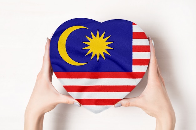 Bandiera della Malesia su una scatola a forma di cuore in mani femminili.