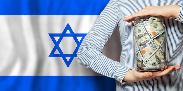 Bandiera ebraica di Israele su uno sfondo di banconote in dollari Concepto della relazione della moneta israeliana in relazione al dollaro l'economia del paese finanziaria