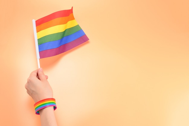 Bandiera LGBT in mano della donna su sfondo arancione. Copia spazio.