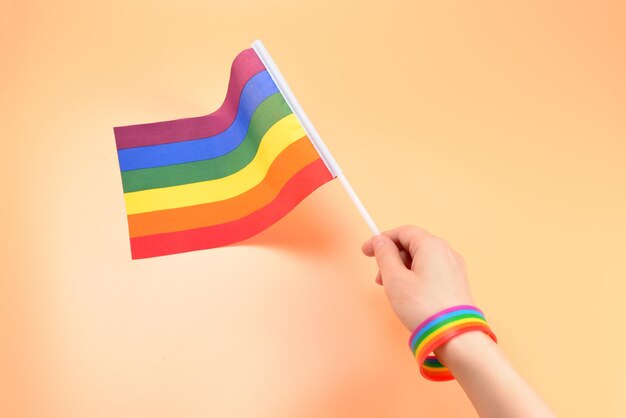 Bandiera LGBT in mano di donna su sfondo arancione. Copia spazio.