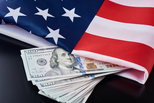 Bandiera nazionale USA e banconote da un dollaro su uno sfondo scuro. Concetto di affari e finanza