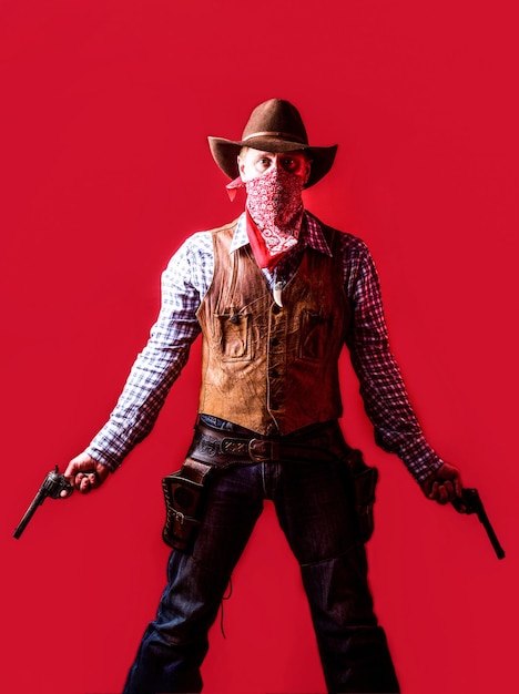 Bandito americano in maschera uomo occidentale con cappello Uomo che indossa un cappello da cowboy pistola Pistole occidentali Ritratto di un cowboy owboy con arma su sfondo rosso