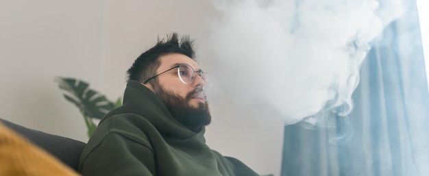 Banner barbuto uomo sta fumando narghilè a casa e soffiando nuvola di fumo copia spazio chill time e re