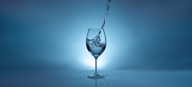 Banner con versando acqua in un bicchiere trasparente per vino. sfondo azzurro con spruzzi d'acqua e copia spazio